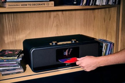 Impianto hi-fi nero con pulsanti dorati e inserimento di un CD sul pannello frontale, su uno scaffale circondato da dischi