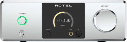 Srebrny aluminiowy przedwzmacniacz słuchawkowy hi-fi Rotel Dx-3, widok z przodu, prostokątny panel z centralnym czarnym wyświetlaczem z cyfrowym wskaźnikiem, okrągły przycisk zasilania z zielonym podświetleniem i trzystopniowy selektor wzmocnienia po lewej stronie, duże metalowe pokrętło głośności po prawej stronie