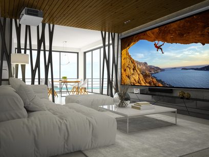 Moderne stue med hvid sofa, sofabord, panoramaudsigt over hav og klipper gennem glasvæg, vægmonteret skærm der viser klatrer på klippefuld klippe