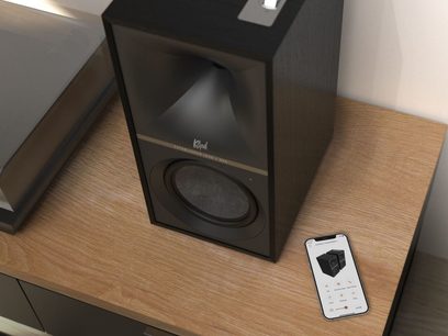 Kabellose, vernetzte Klipsch The Sevens Lautsprecher in Schwarz, Frontalansicht in Großaufnahme, mit Fernbedienung auf Holzmöbel