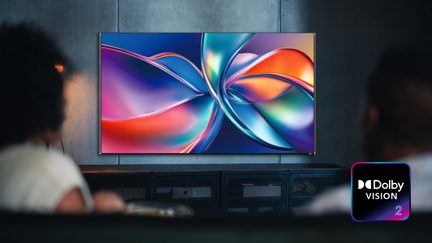 Černý nástěnný televizor s tenkým kovovým rámem, pohled zepředu, abstraktní vícebarevný obraz, logo Dolby Vision vpravo dole