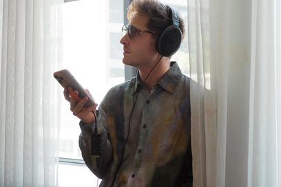Convertor audio portabil Questyle M18i conectat la un smartphone ținut de un bărbat cu căști lângă o fereastră