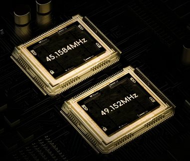 To gyldne elektroniske chips 45,1584 MHz og 49,152 MHz på sort printkort, set i perspektiv