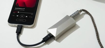 Hvid smartphone med tændt skærm, sort flettet kabel, sølvfarvet lydtilslut, oversigt fra oven