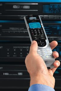 Univerzální dálkový ovladač Logitech Harmony 525 v šedé a stříbrné barvě, držený v ruce, pohled zepředu, zapnutý LCD displej