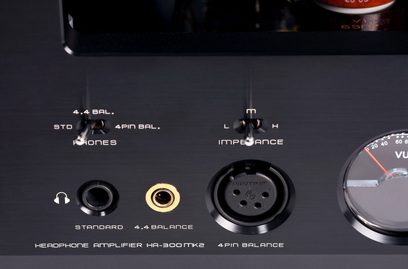 Primo piano frontale sulla facciata in alluminio spazzolato nero del preamplificatore per cuffie hi-fi Cayin HA-300MK2, che mostra due interruttori metallici, le prese cuffie da 6,35 mm, 4,4 mm e XLR a 4 poli, oltre a un VU-metro parzialmente visibile