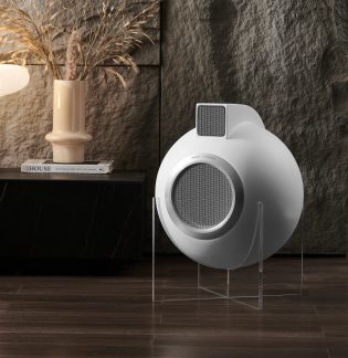 Hvid sfærisk højttaler på gennemsigtigt stativ, sort møbel med beige vase og bog, grå tekstureret væg, trægulv