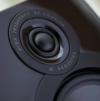 Close-up front view of a circular black speaker with a black acoustic diaphragm in the center and "Q Acoustics" inscription around it
