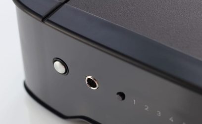 Tæt på det bageste venstre hjørne af en sort Rega Brio hi-fi stereoforstærker, der viser to jackstik og en hvid LED-lampe