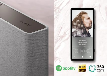 Pilkos kolonėlės vaizdas iš kampo su logotipu viršuje, juodas išmanusis telefonas, rodantis muzikos programėlę, „Spotify“, „Hi-Res Audio“, „360 Reality Audio“ logotipai.