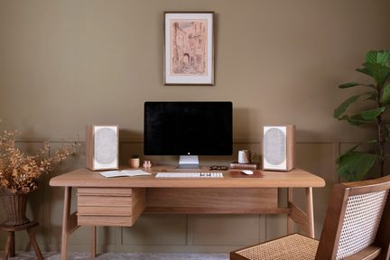 Light wood desk with computer, speakers, mug, glasses, and framed drawing of a medieval street on the wall