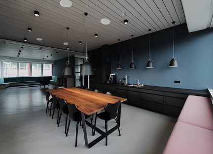 Sala con tavolo in legno, 8 sedie nere, panca rosa, cucina nera, 7 sospensioni nere, soffitto rivestito in legno, finestre a sinistra