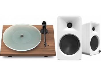 Giradischi in finitura legno con piatto trasparente e braccio nero, accompagnato da due diffusori bianchi con altoparlanti neri