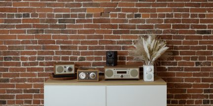 Namizni radijski sprejemniki Tivoli Audio v vintage dizajnu iz svetlega lesa in bele barve na modernem bufetu pred zidom iz rdeče opeke