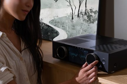 Černý stereo hi-fi zesilovač Onkyo na dřevěném nábytku, ženská ruka nastavuje velké otočné tlačítko hlasitosti