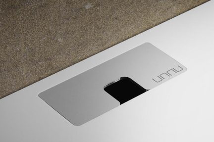 Obdélníkový kartáčovaný kovový prostup pro kabely na bílém stolovém plátu, černý otvor, logo „UNNU“, pohled shora