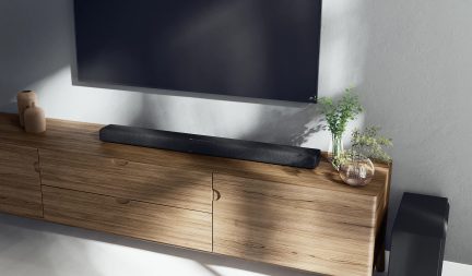 Ljust trämöbel för TV med svart soundbar, dekorativa vaser och grön växt, släckt TV-skärm på väggen