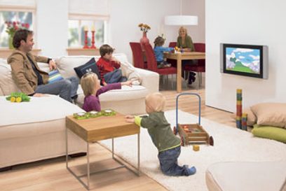 Moderne stue med familie, der ser fjernsyn, beige sofaer, træbordplade, legetøj på gulvet, store vinduer