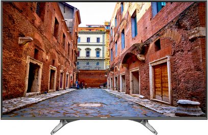Televisão Panasonic TX-40DX600E exibindo uma viela pavimentada estreita ladeada por velhos edifícios de tijolos vermelhos, vista frontal
