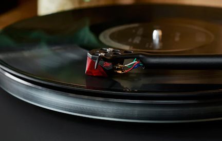 Platine vinyle noire avec bras de lecture et cellule rouge et verte, gros plan en vue de dessus légèrement inclinée