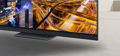 Tv TCL 75X925 set forfra, tændt skærm viser en oplyst motorvej om natten, tynd sort ramme
