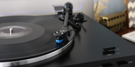 En sort pladespiller med en sort vinylplade, en tonearm med en blå pickup og en størrelsesvælger til 12" eller 7".