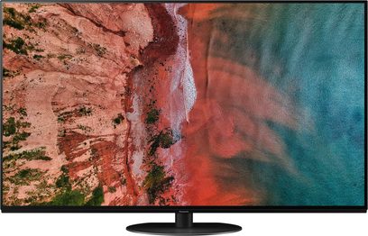 Téléviseur Panasonic TX-55HZ1000E affichant une vue aérienne d'une plage rocheuse rouge contrastant avec l'océan bleu-vert