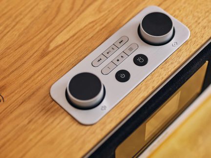 betjeningspanel til bluetooth-højttaler i lyst trædesign og børstet metal med to drejeknapper og multimedieknapper