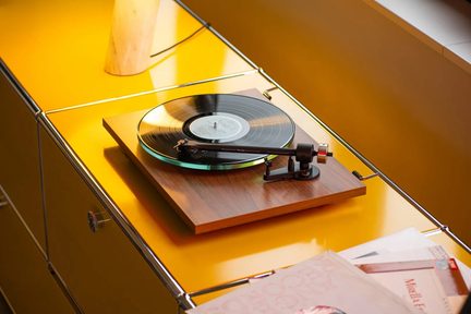 Tocadiscos de vinilo con acabado de madera, con disco negro y brazo de lectura, vista en ángulo sobre mueble amarillo brillante