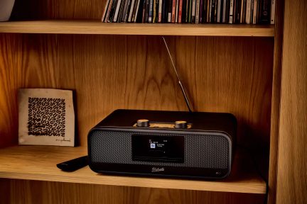 Sort Roberts-radio med centralt display, gyldne knapper og teleskopantenne, på en hylde
