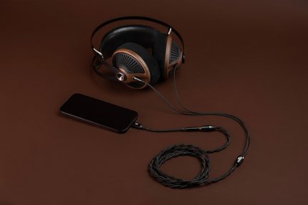 Sluchátka s obepínajícími ušními mušlemi z hnědého dřeva a černého kovu s černými koženkovými polstrováními, černý opletený audio kabel připojený k černému smartphonu, pohled shora