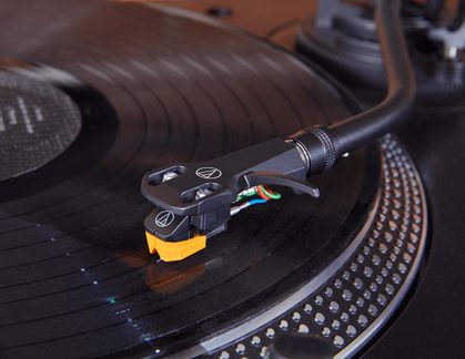 Gramofon Audio-Technica, detail raménka přenosky s oranžovým diamantem na černé vinylové desce