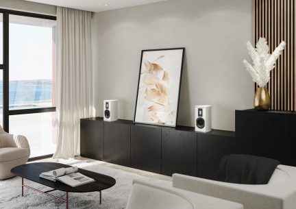 Pair of white bookshelf speakers on a long black cabinet in a bright modern living room with minimalist decor