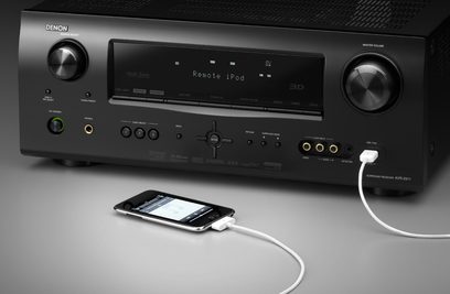 Denon AVR-2311 sort hjemmebiografsforstærker, set forfra, blå skærm, knapper og drejeknapper, tilsluttet en hvid iPhone med kabel