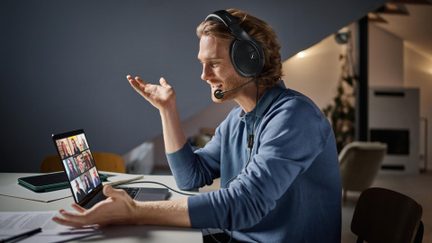 Profil av en mann med svarte, plastikk circum-aurale hodetelefoner med mikrofonbom, foran en bærbar PC på videoanrop