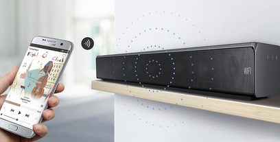 Sort Samsung HW-MS651 soundbar, set forfra, og smartphone der viser "Fish Clock"-appen i forgrunden