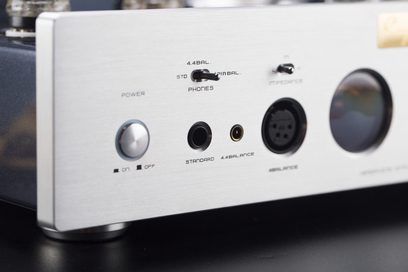 Trekvart forfra-visning af en sort Cayin HA-6A hovedtelefonforforstærker, metalkabinet med sølvfarvet børstet aluminiumfront, rund tænd/sluk-knap, miniaturevælgere, 6,35 mm og 4,4 mm hovedtelefonudgange, 4-polet XLR-stik og cirkulært VU-meter