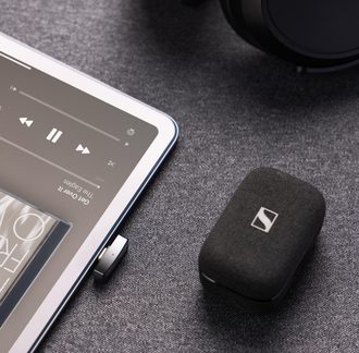 Черно текстилно зарядно калъфче за безжични слушалки Sennheiser, отблизо до таблет по време на възпроизвеждане на аудио