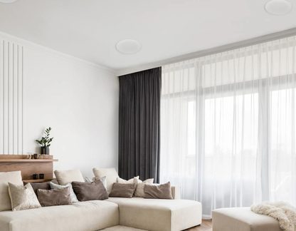 Møntsalong, hjørnesofa i beige stof med taupe puder, hylde i træ, stort vinduesparti, hvidt gardin, gråt forhæng