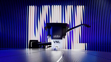 Célula fonográfica preta e branca de plástico sobre disco de vinil, agulha abaixada, vista frontal em close-up, inscrição “VNL”