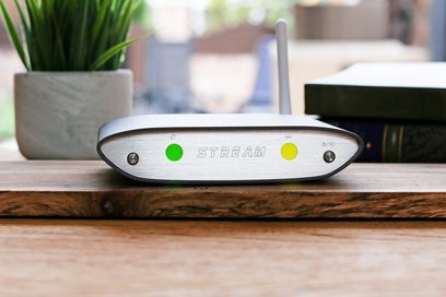iFi Audio Zen Stream netværksaudioafspiller i sølvfarve, nærbillede forfra på et træbord, to grønne LED'er lyser