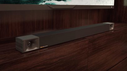 Zwarte Klipsch Cinema 800 soundbar, vooraanzicht, geplaatst op een donkere houten kast voor een scherm met een golfpatroon