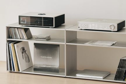 Estantería metálica rectangular con 6 compartimentos que contienen vinilos, CD, libros, reproductor de red y amplificador de audio