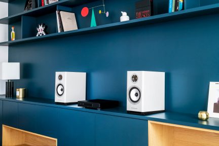 Coppia di diffusori da scaffale Triangle bianchi con amplificatore nero su mobile blu in un soggiorno contemporaneo