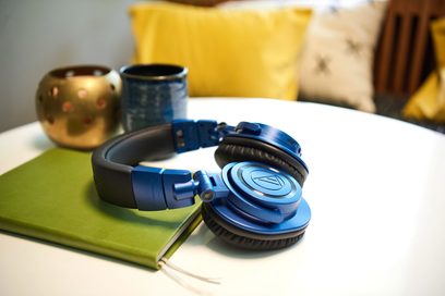 Sluchátka Audio Technica ATH-M50xBT2DS v modro-černé barvě položená na zeleném notesu s dvěma rozmazanými zlatými hrnky v pozadí