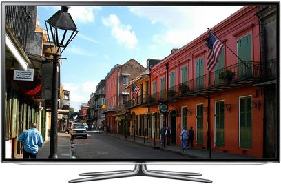 Televizor Samsung UE55ES6530 zobrazující dlážděnou ulici lemovanou barevnými vícepodlažními budovami a lidmi, kteří po ní procházejí