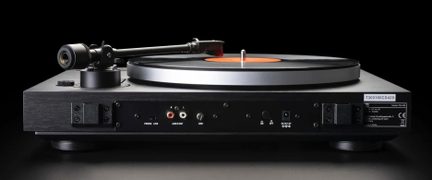 Toca-discos de vinil preto com chassi em acabamento de madeira, prato metálico prateado, vista traseira mostrando conectores de áudio RCA, seletor phono/line, entrada de alimentação DC e braço de leitura em metal