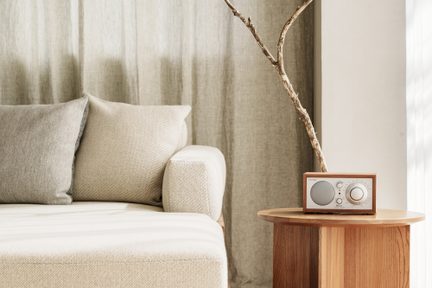 namizni radio Tivoli Audio iz svetlega lesa z velikim okroglim gumbom na hrastovi mizi v bež minimalistični dnevni sobi