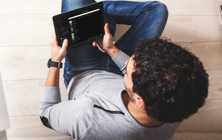 Arkadan yakın çekim görüntülenmiş, bir tableti tutan ve tabletinde bir yazılım gösteren oturan adam