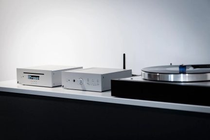Silverfärgad hi-fi-anläggning med ljudspelare, förstärkare och svart skivspelare på vit hylla